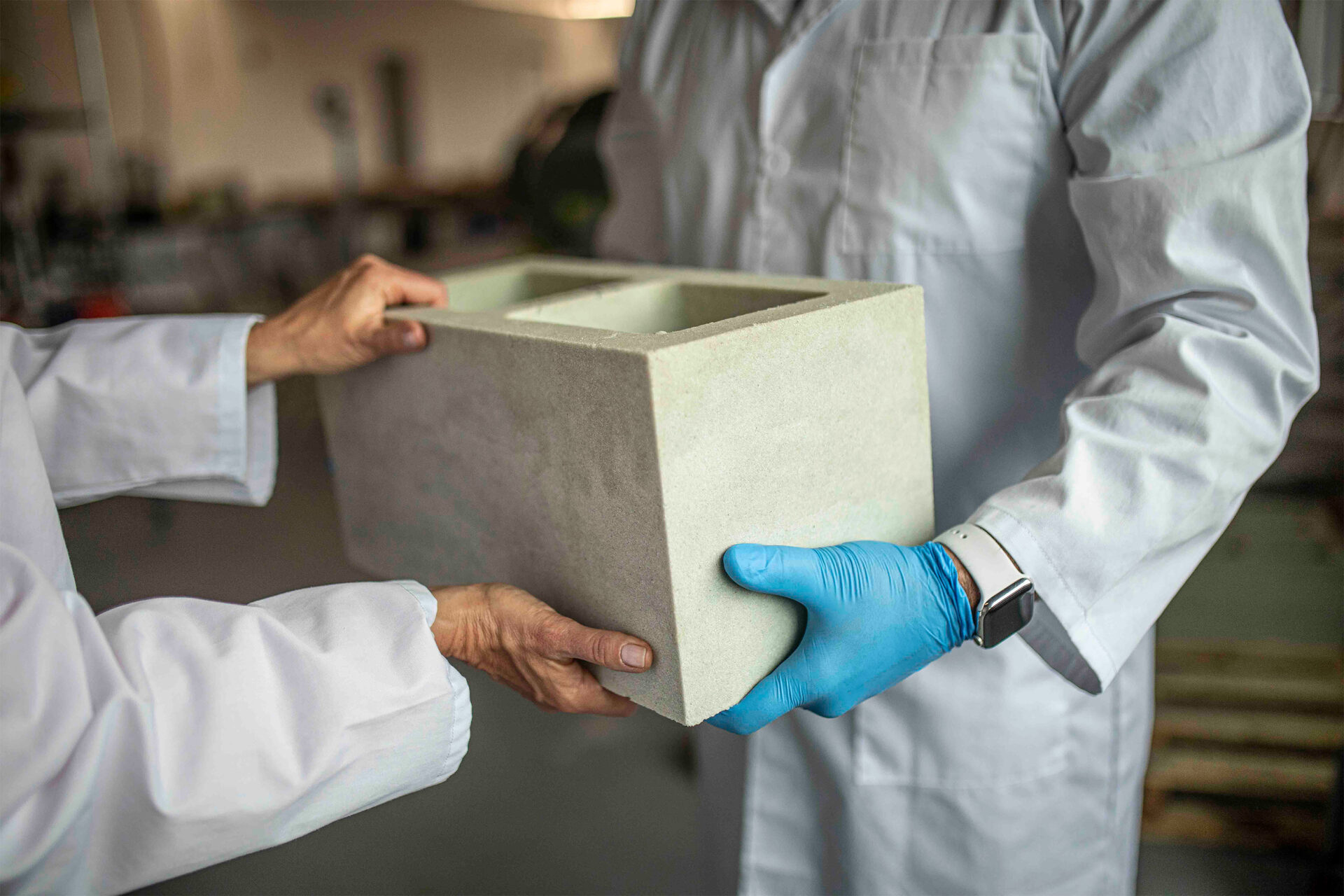 Two sets of hands hold a Prometheus Materials bio-cement brick.