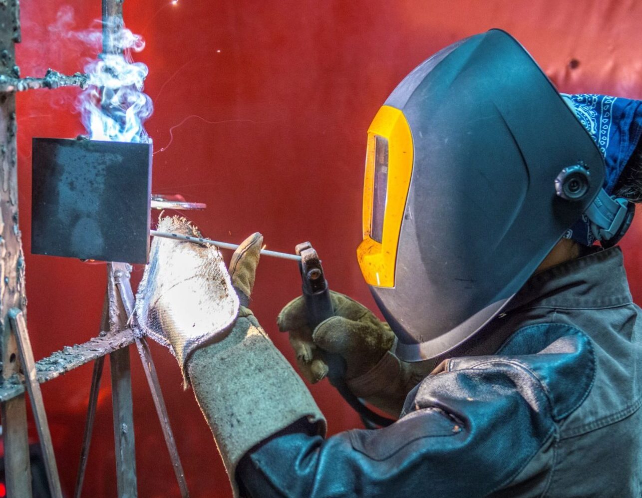 JARC trainee wearing welding PPE (mask, gloves, etc.), welding as part of JARC advanced manufacturing training program.