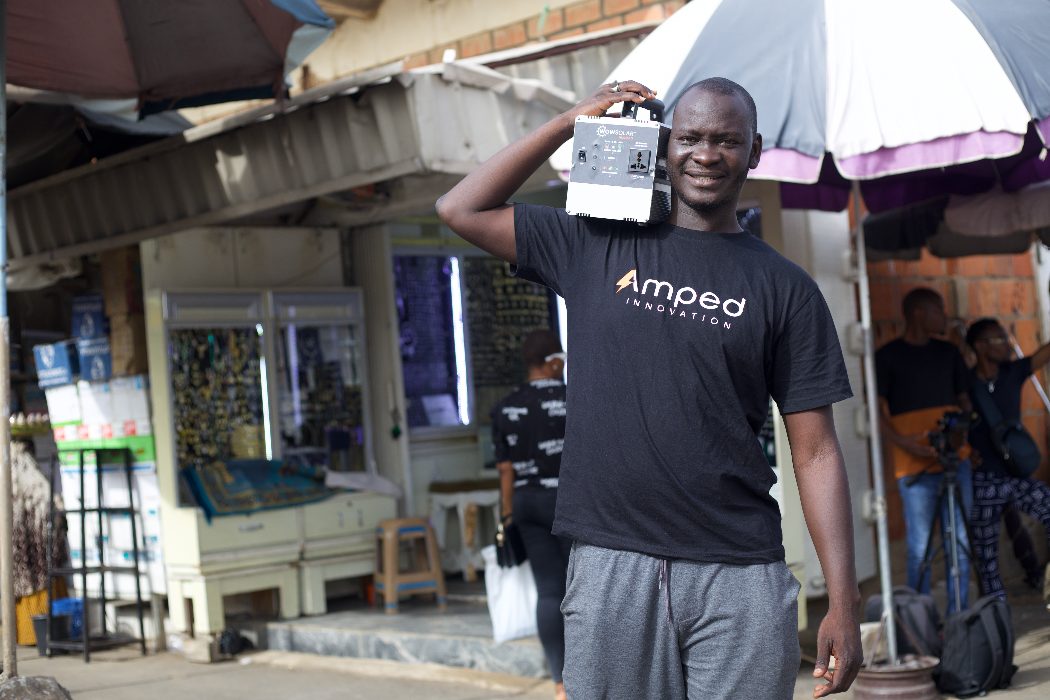 An Amped Innovation staff member carrying one of its solar generators on his shoulder—smiling, wearing black Amped Innovation t-shirt.