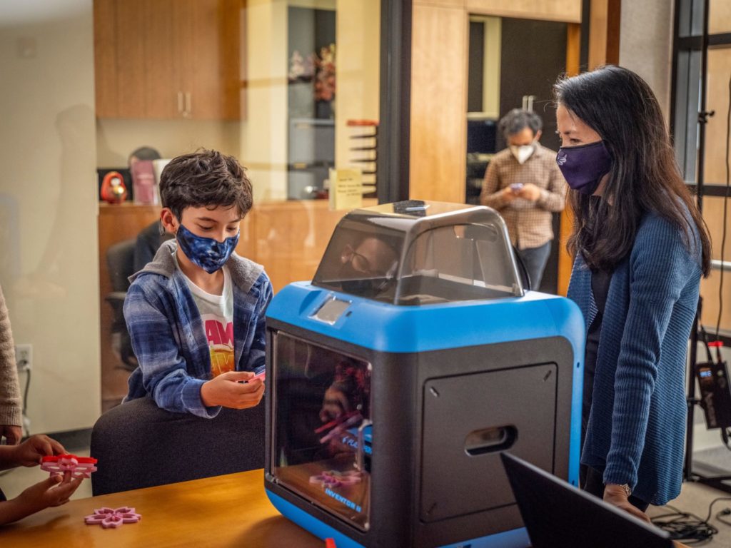 Gail Tanaka, children, and seniors admire 3D printed cherry blossoms at KImochi