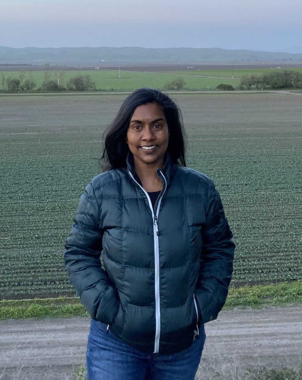 Autodesk employee Amanda Brijpaul stands in a field at dusk wearing a down jacket