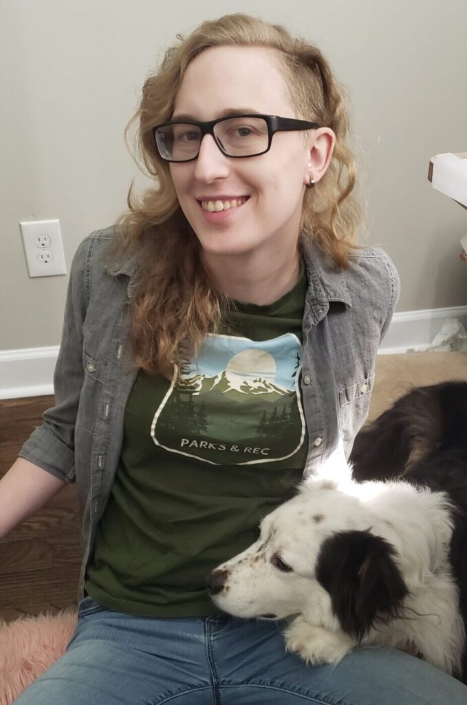 Autodesk employee Rachel Schnaubelt sits on the ground with a black-and-white dog.