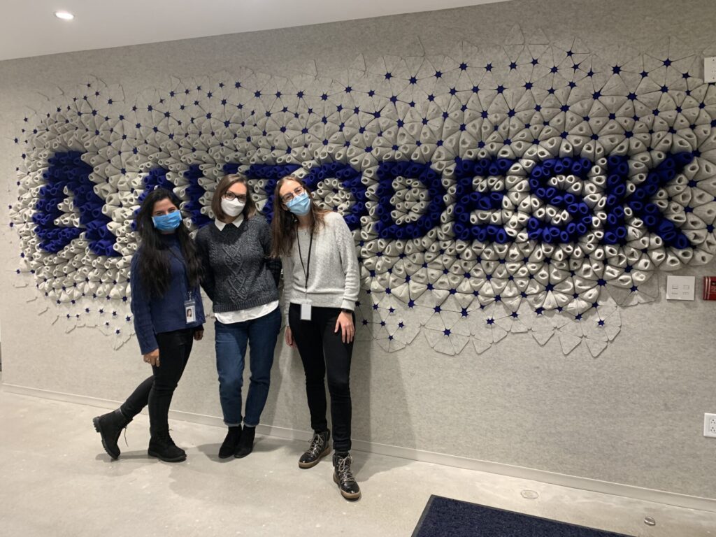 Kaveri Joshi stands to the left of two female colleagues in front of a mural of the Autodesk logo.