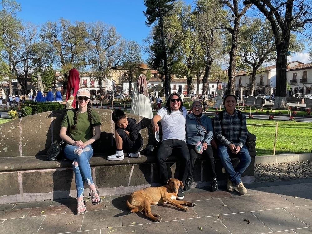 Jose Bravo sits with his family on a bench in a park in Mexico. A brown dog lies on the ground next to Jose's feet.