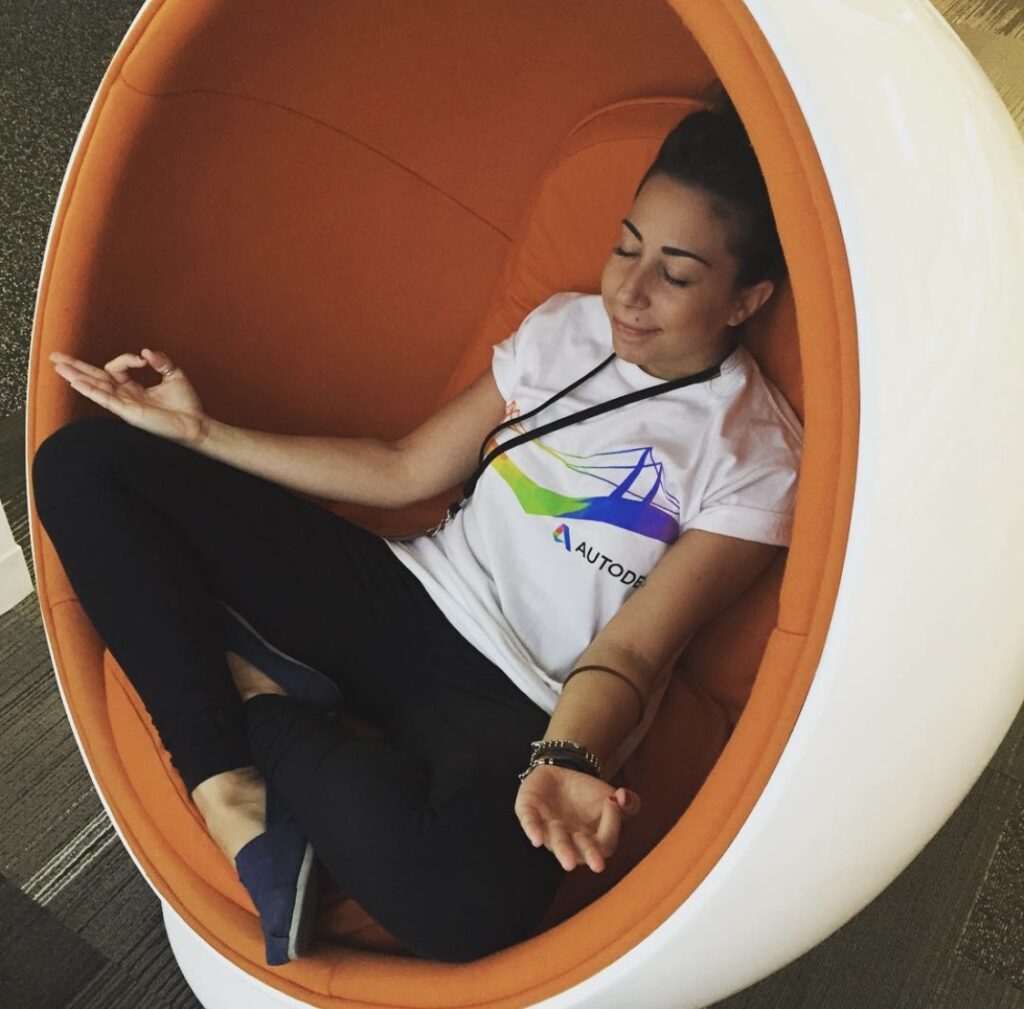 Autodesk employee Lisa Ferliano sits in a white and orange circular pod, the tips of her thumbs and index fingers touching while practicing meditation