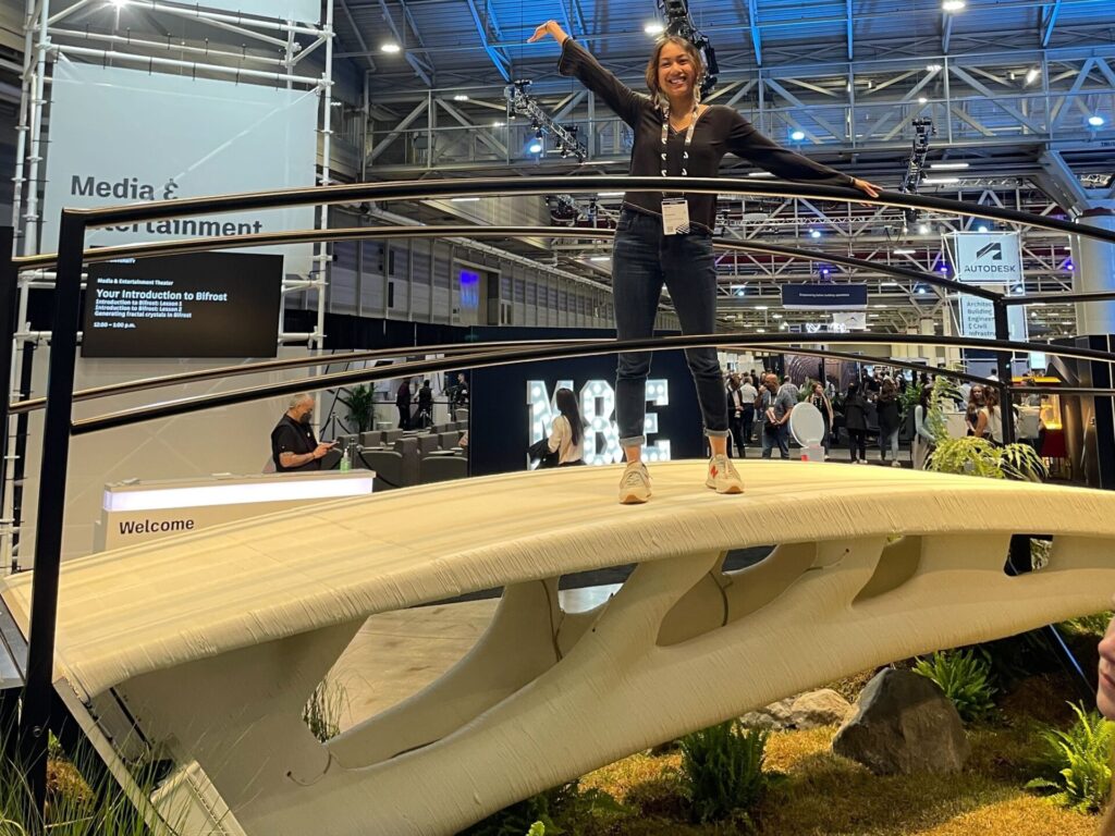 In the expo hall at Autodesk University, a woman stands on a small pedestrian bridge that was built using a 3D printer.