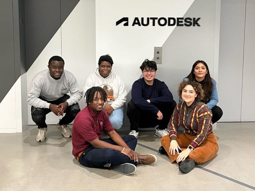 SMASH Rising interns sit on the floor in front of an elevator with the Autodesk logo on the wall