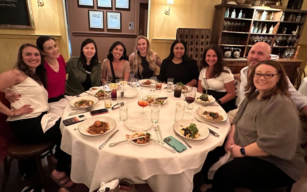 A group of nine Autodesk employees sits at a round table in a restaurant with plates of local New Orleans cuisine.