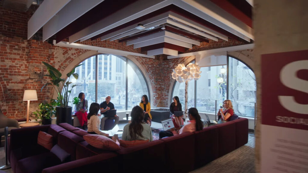 Eight Autodesk employees talk to each other while sitting on a purple sectional couch