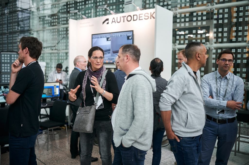 Picture of people standing and talking by Autodesk information booths. 