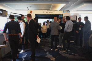 Group of people standing at an exhibition of technology booths.