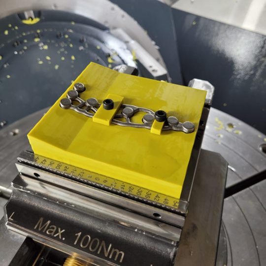 Generative HTO plate clamped to the custom resin fixture for machining holes and threads.