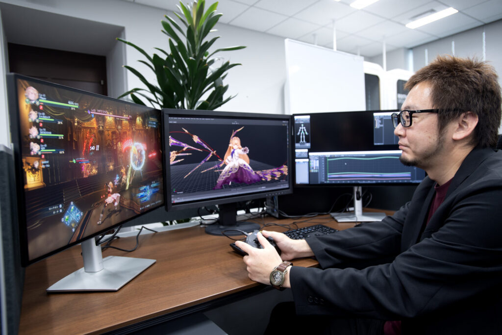 Image of Yasui at his desk undergoing game development with a controller in hand